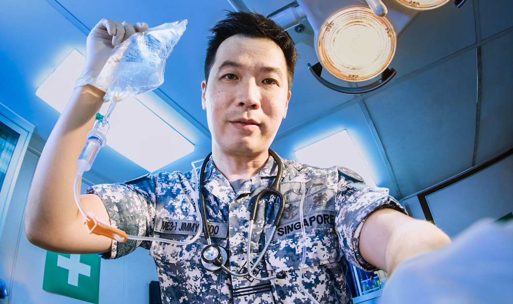 Navy medical expert is holding up an IV drip, and appears to be in the middle of a medical procedure